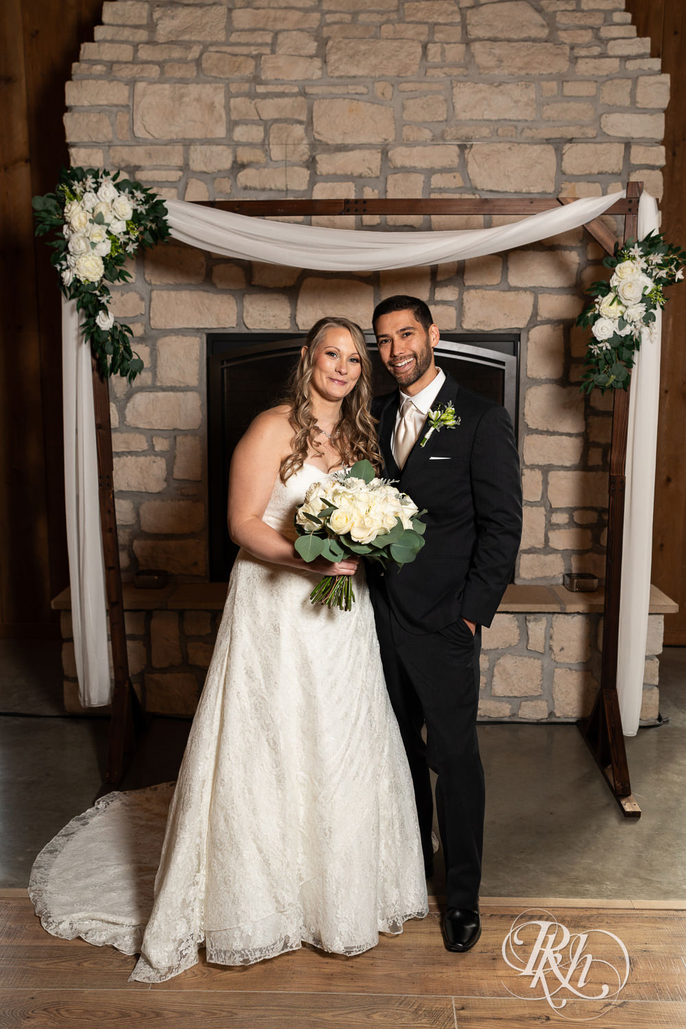 Bride and groom smile in front of a fireplace at Almquist Farm in Hastings, Minnesota.