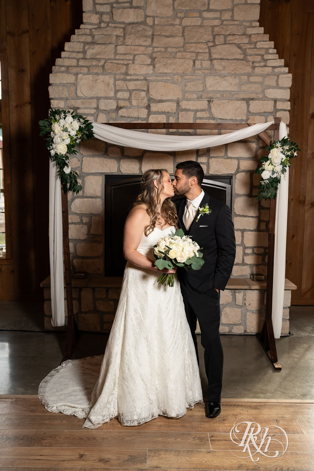 Bride and groom kiss in front of a fireplace at Almquist Farm in Hastings, Minnesota.