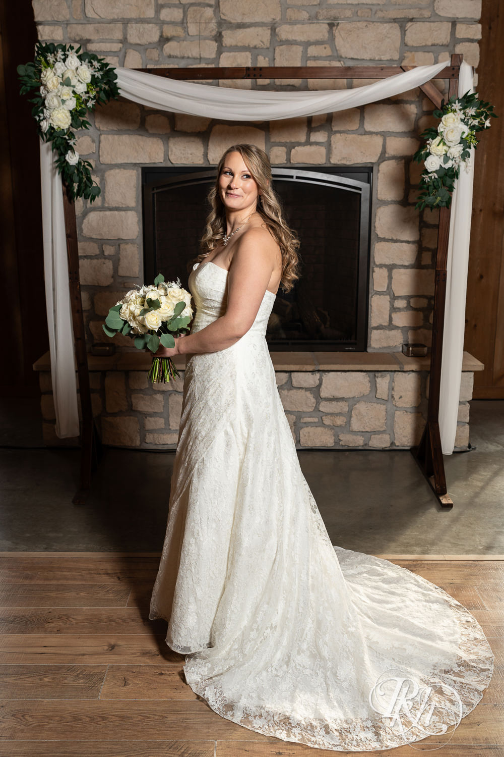 Bride smiles in front of a fireplace at Almquist Farm in Hastings, Minnesota.