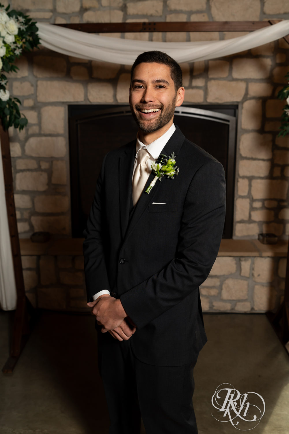Groom smiles in front of a fireplace at Almquist Farm in Hastings, Minnesota.