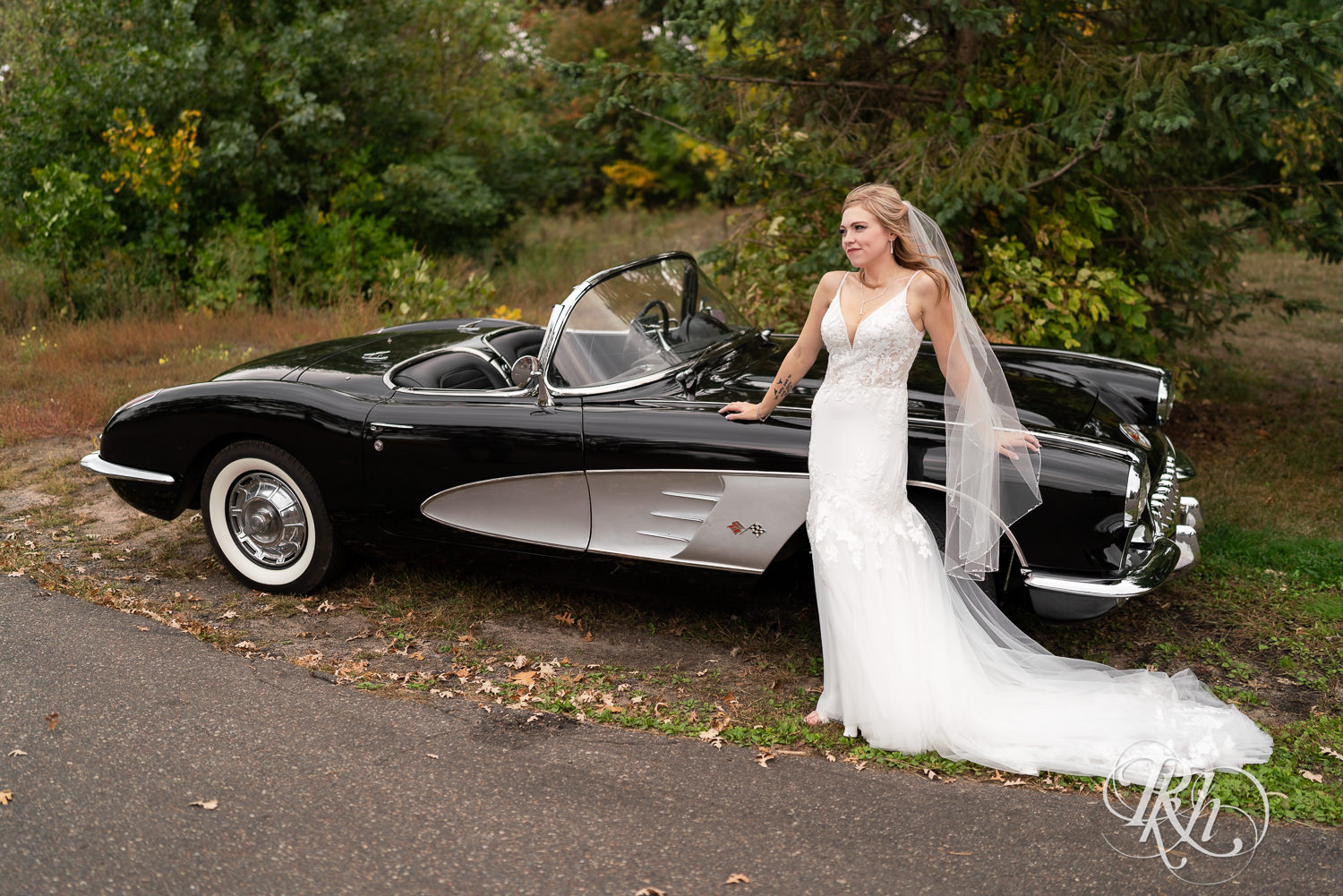Bride smiles in front of a vintage Corvette at Bunker Hills Event Center in Coon Rapids, Minnesota.