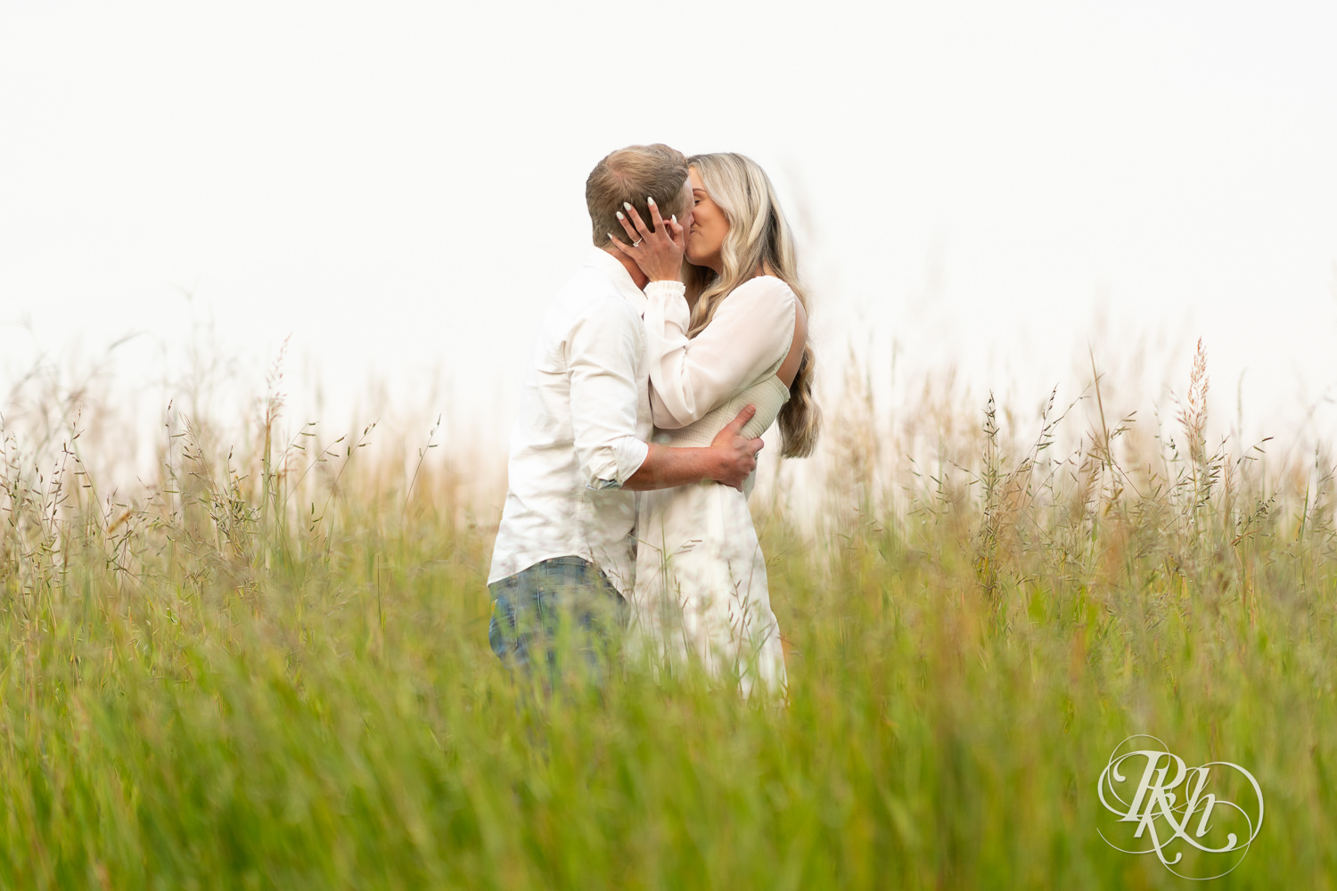 Man and woman in white and cowboy boots kiss in open field engagement photos at Lebanon Hills Regional Park in Eagan, Minnesota.