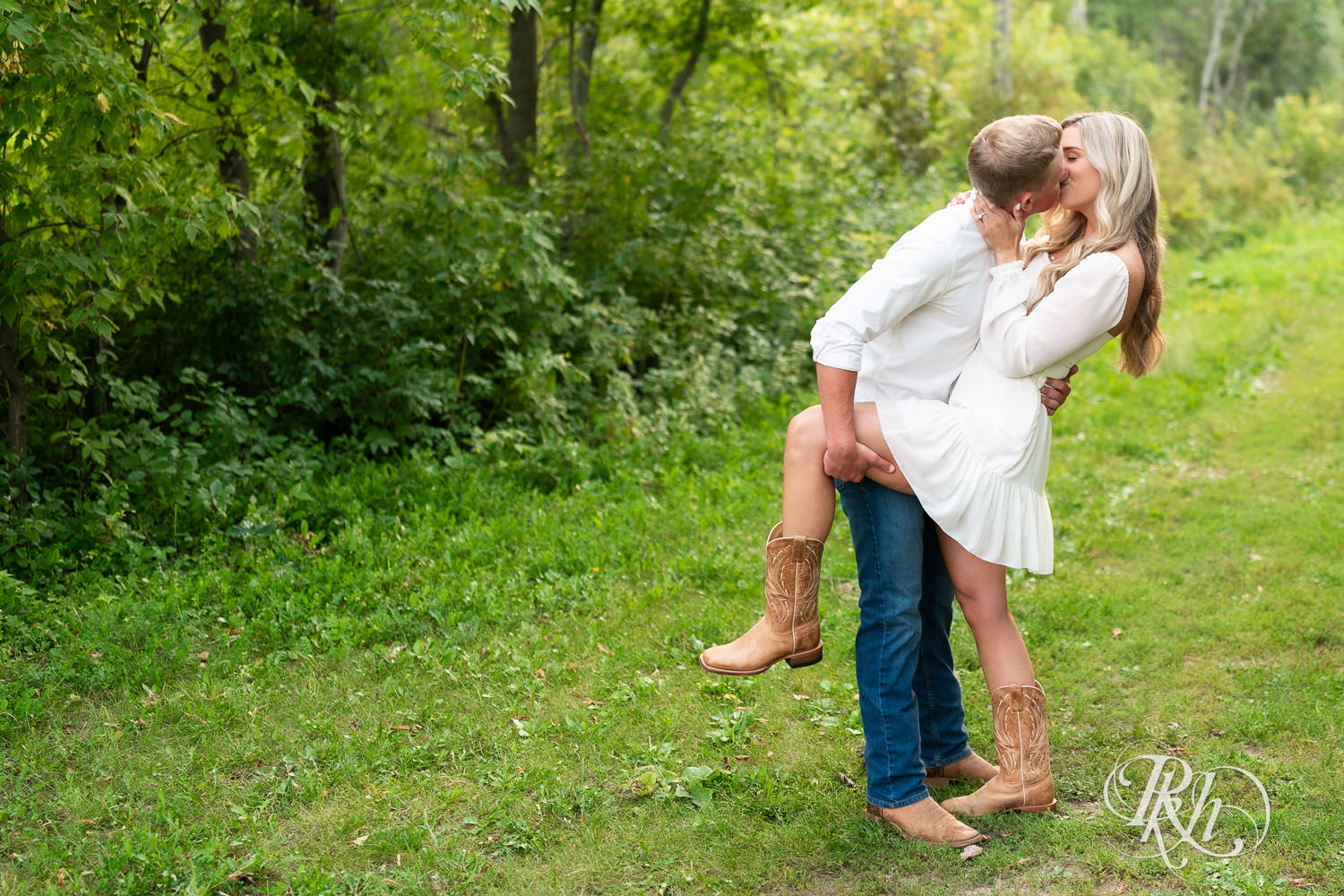 Man and woman in white and cowboy boots kiss in a field at Lebanon Hills Regional Park in Eagan, Minnesota.