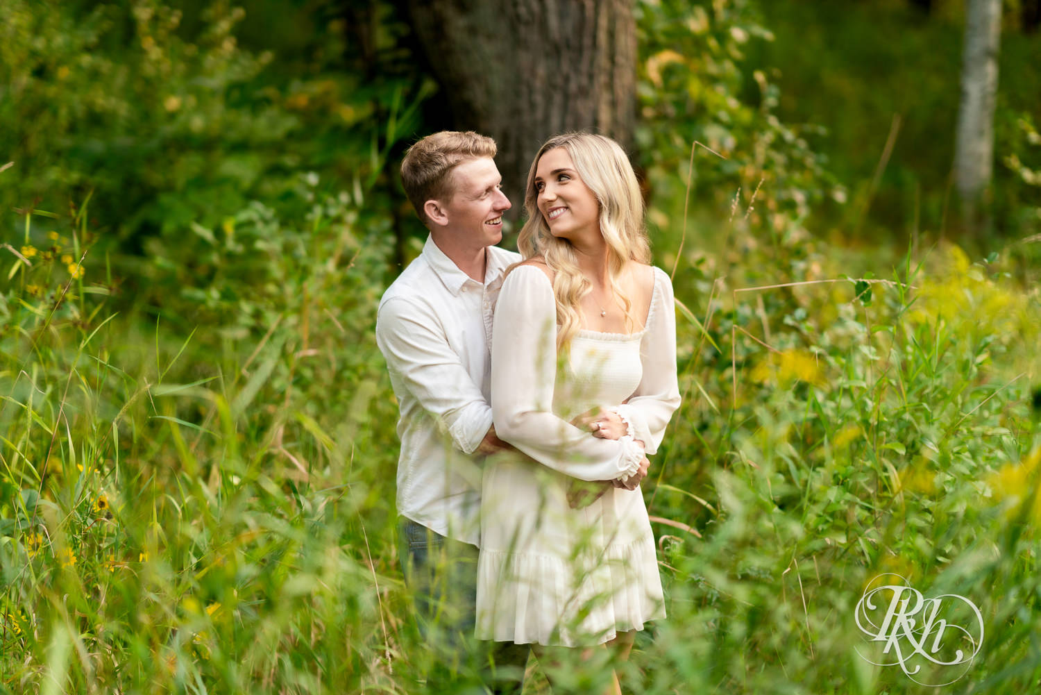 Man and woman in white and cowboy boots smile during engagement photography at Lebanon Hills Regional Park in Eagan, Minnesota.