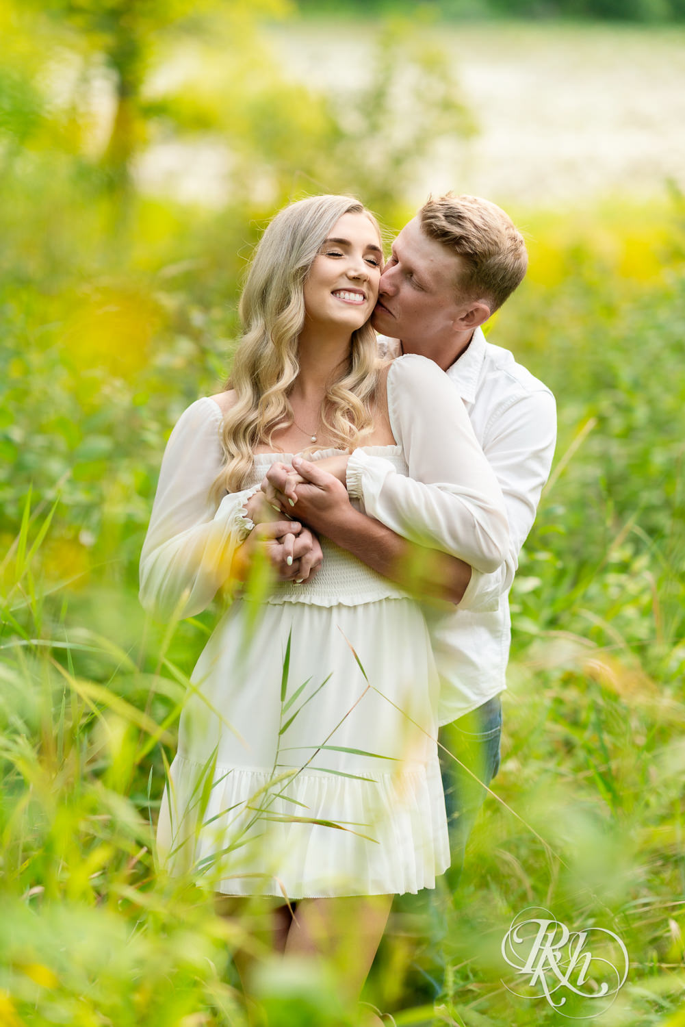 Man and woman in white and cowboy boots kiss during open field engagement photos at Lebanon Hills Regional Park in Eagan, Minnesota.