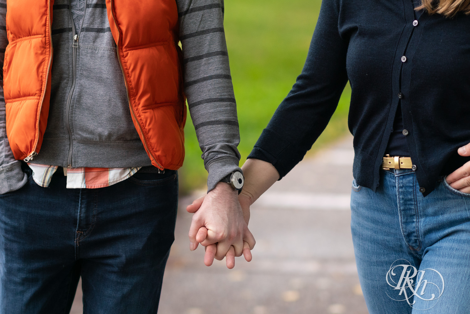 Man and woman in hoodies and jeans hold hands during rainy engagement photos at Boom Island Park in Minneapolis, Minnesota.