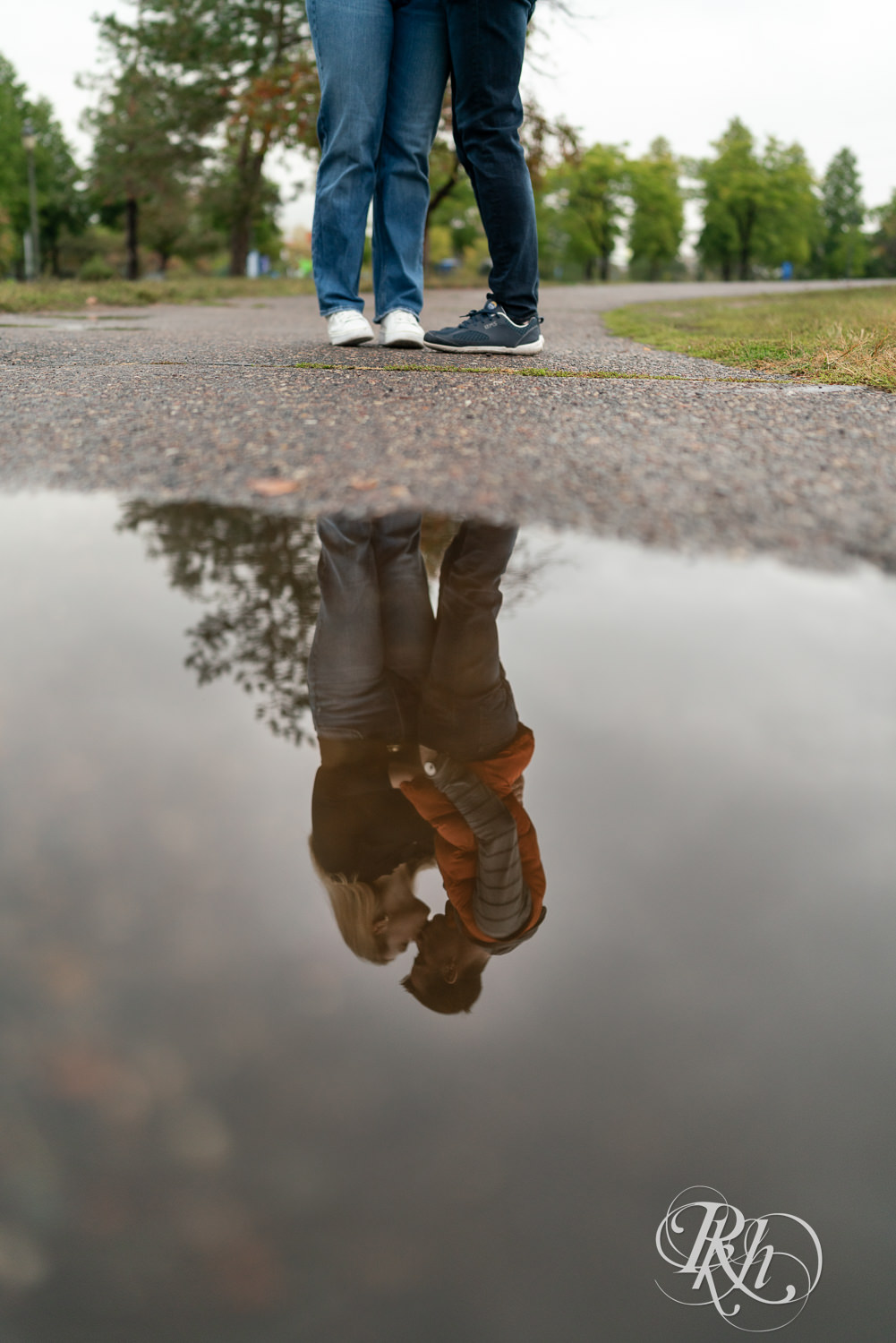 Man and woman in hoodies and jeans kiss during rainy engagement photos at Boom Island Park in Minneapolis, Minnesota.