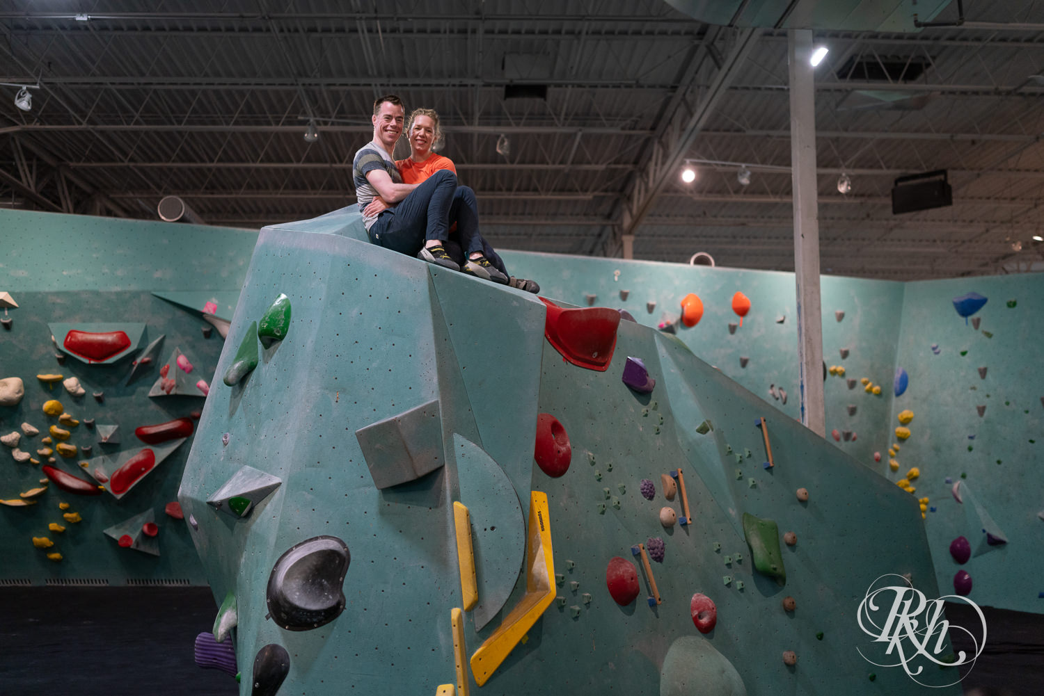 Man and woman rock climb during engagement photography session at the Bouldering Project in Minneapolis, Minnesota.