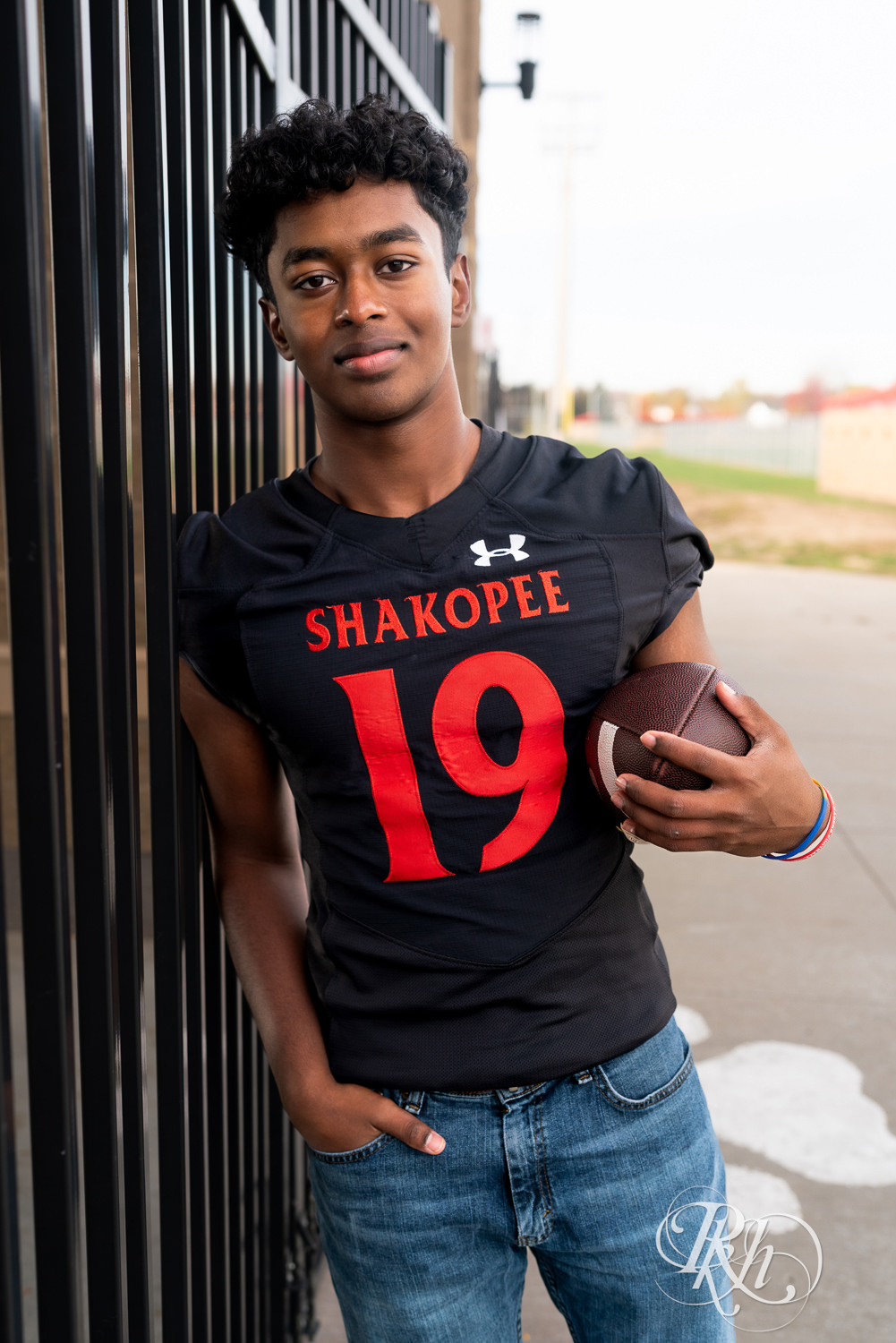 Indian senior boy poses with football at Shakopee High School for senior photography.