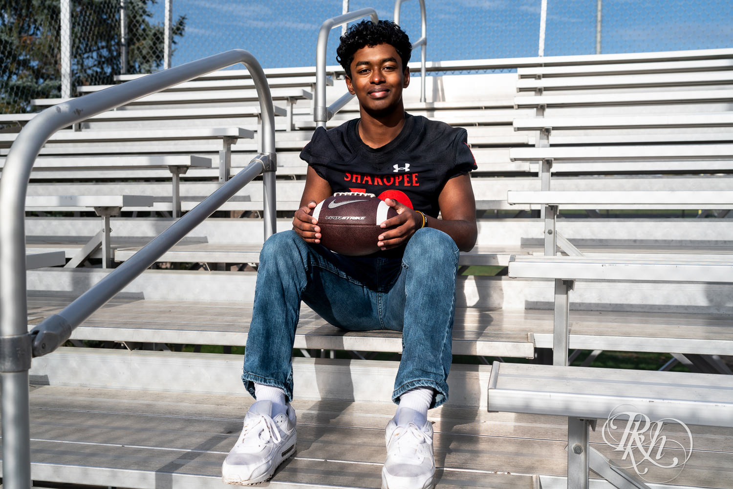 Indian senior boy poses with football at Shakopee High School for senior photography.