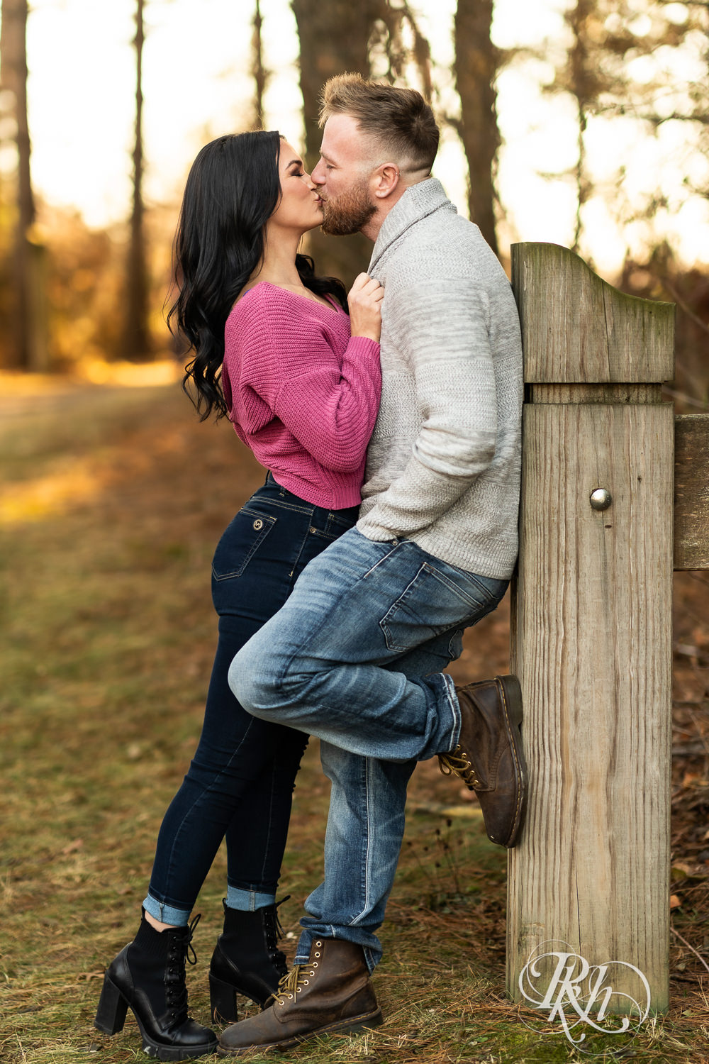 Man in sweater and jeans lifts and woman in pink sweater and jeans kiss at Lebanon Hills Regional Park in Eagan, Minnesota.