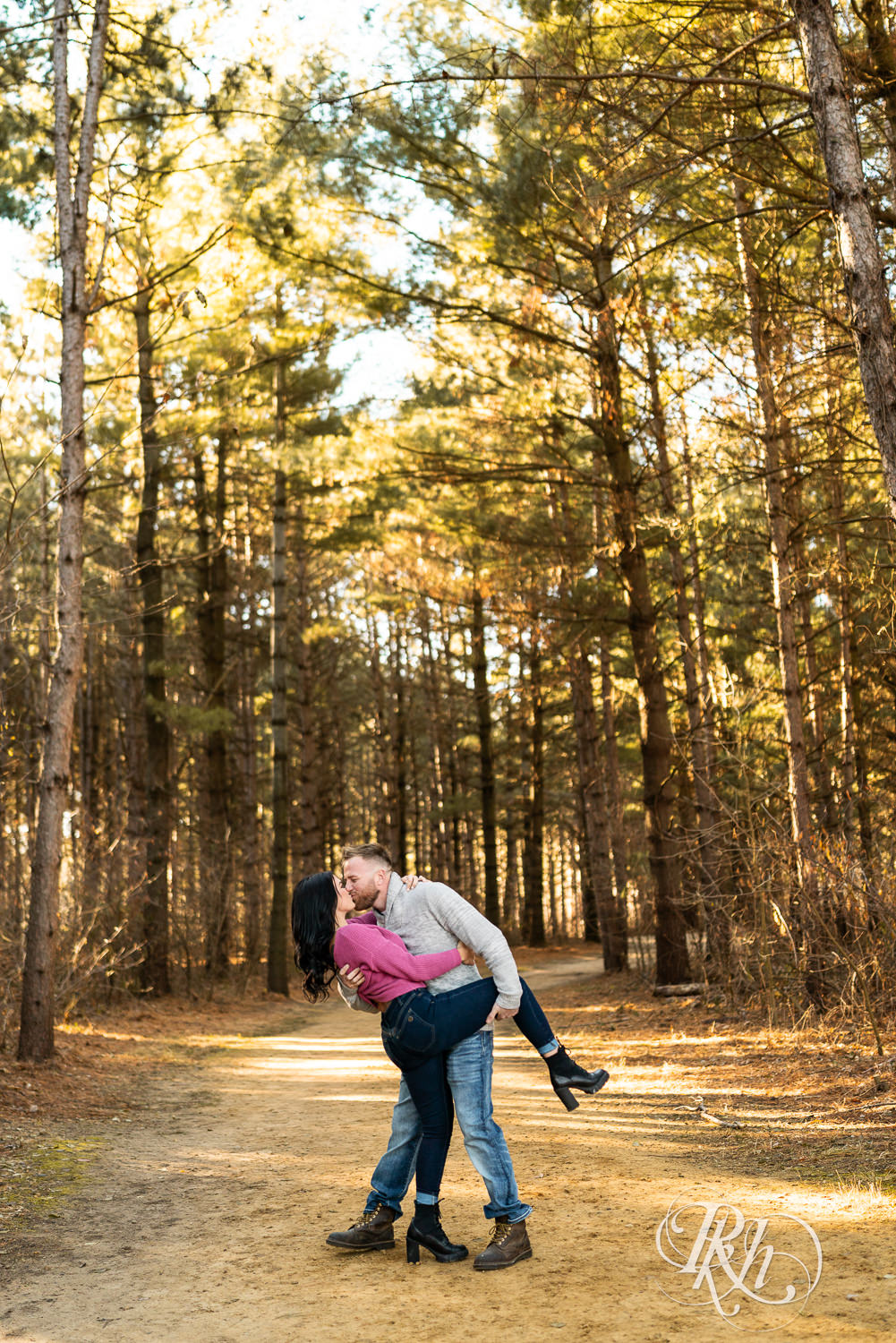Man in sweater and jeans and woman in pink sweater and jeans kiss in woods at Lebanon Hills Regional Park in Eagan, Minnesota.