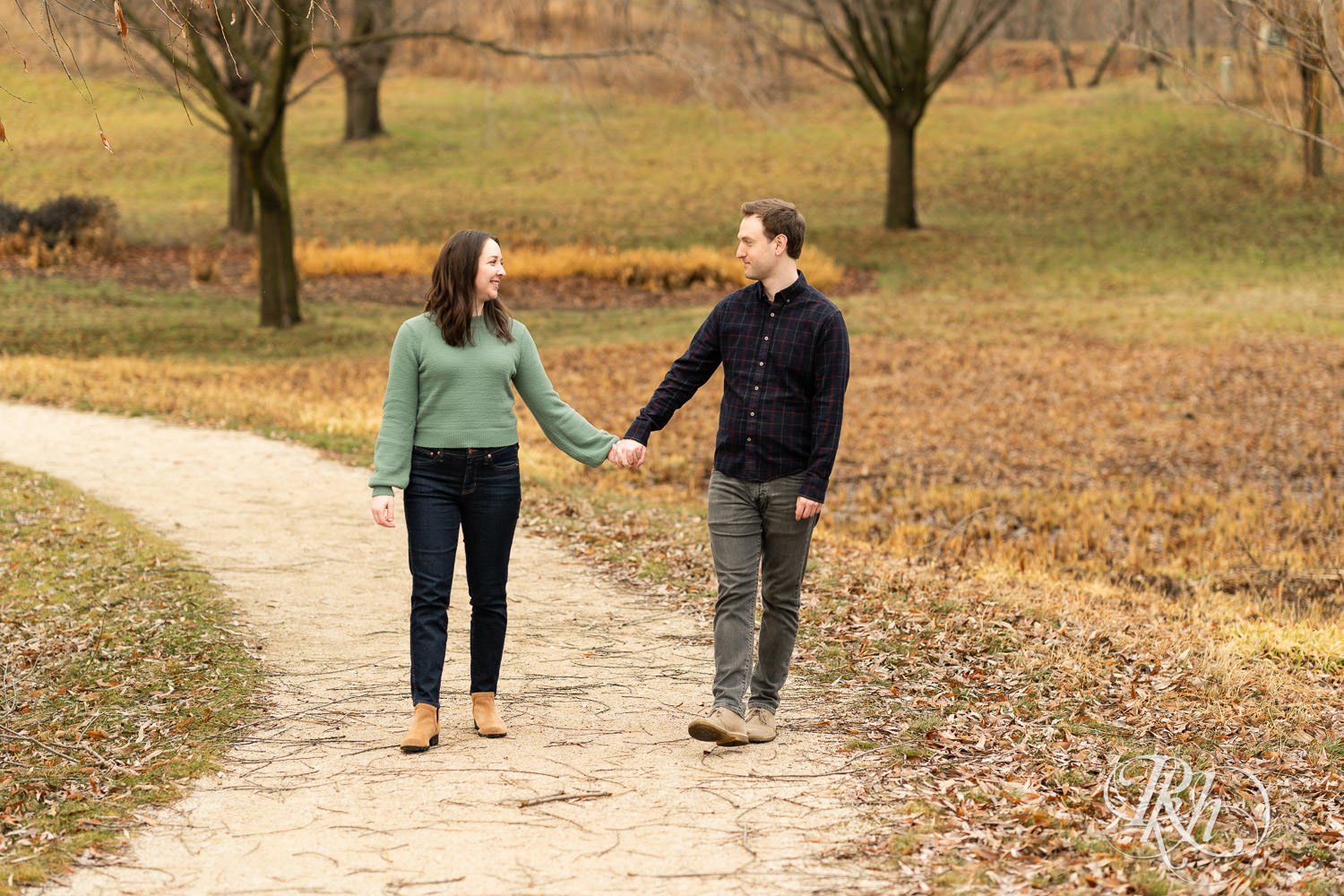 Man and woman walk holding hands during winter engagement photography at Minnesota Landscape Arboretum in Chaska, Minnesota.