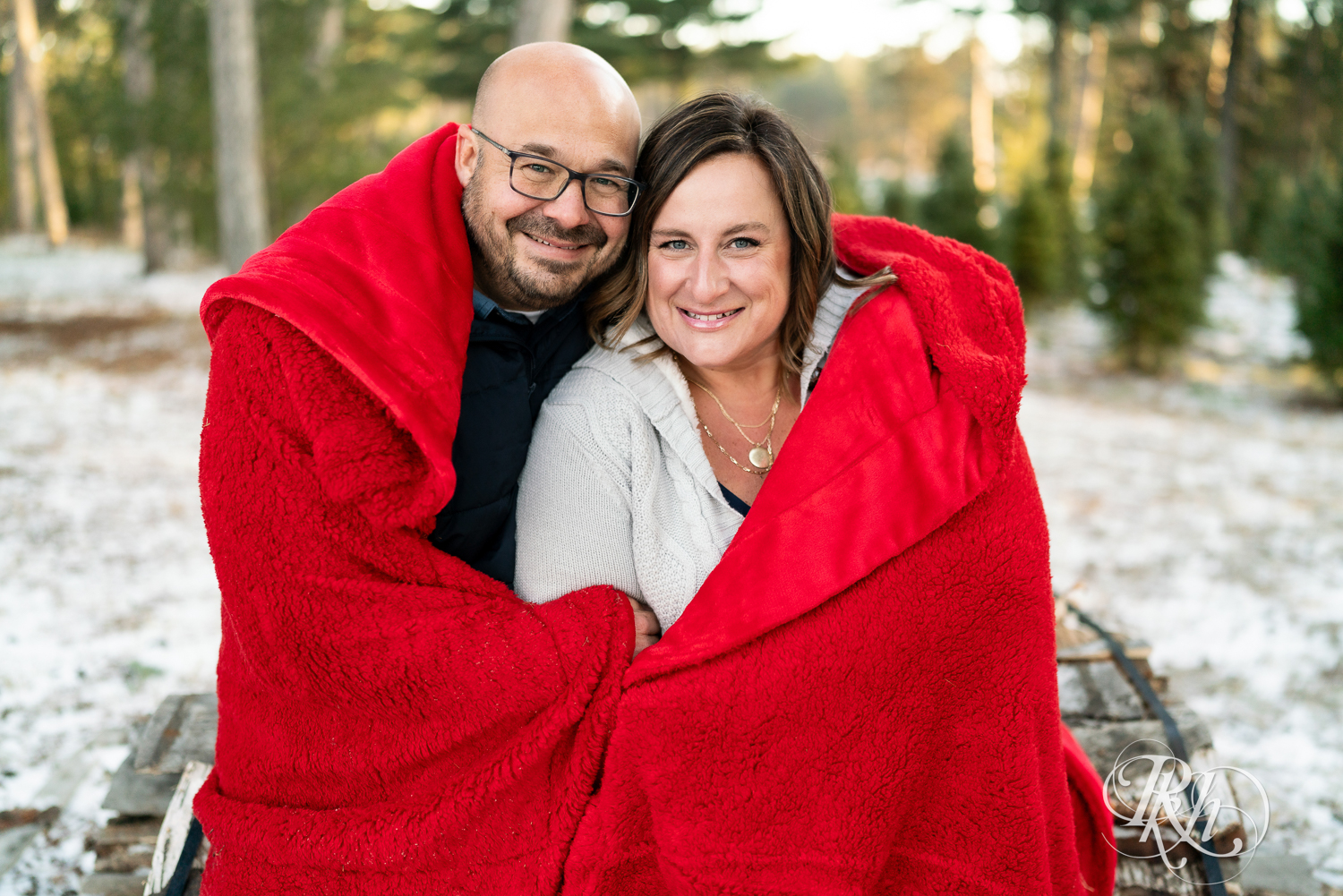 Black man and white woman snuggle in red blanket at Hansen Tree Farm in Anoka, Minnesota.