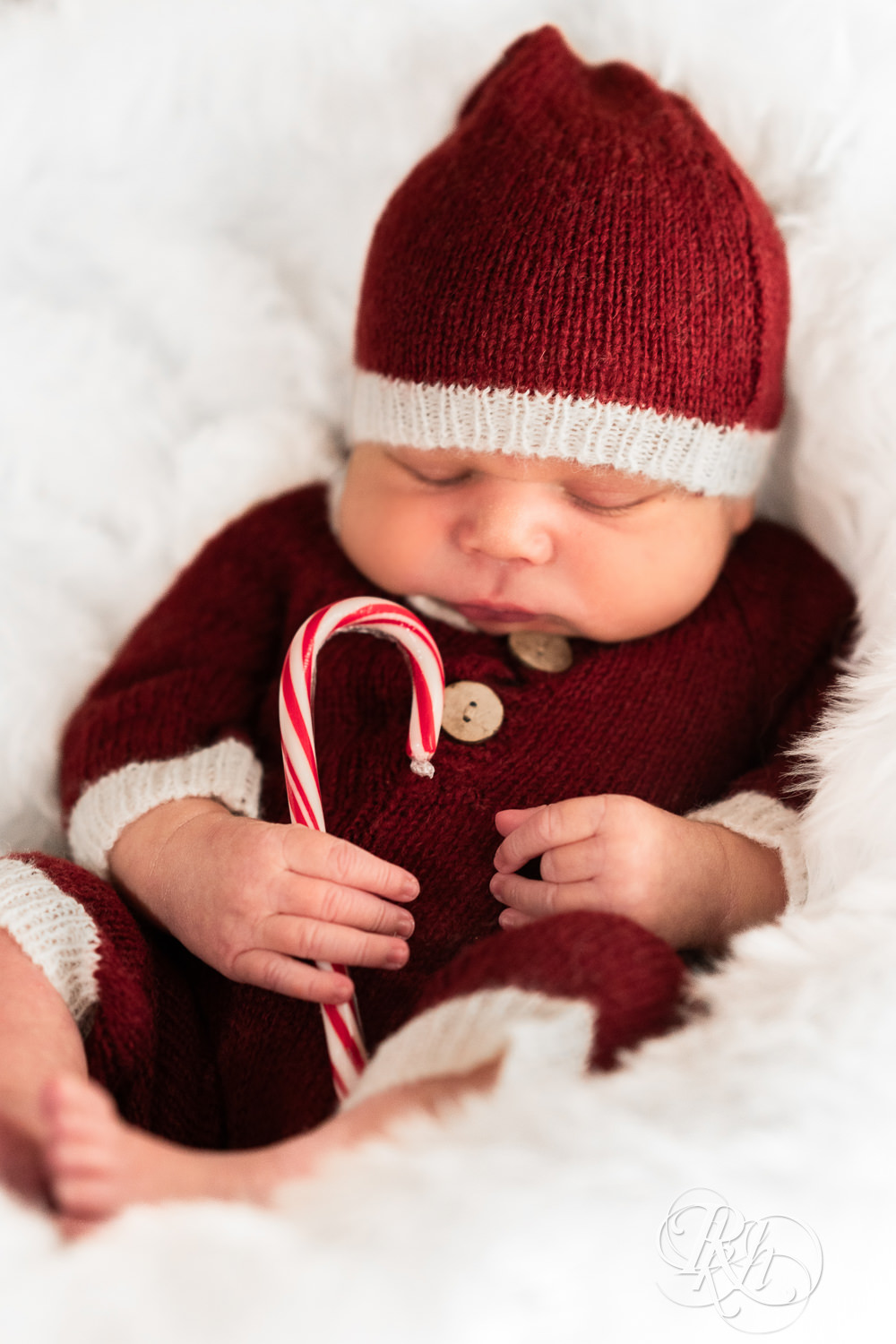 Biracial baby dressed in Santa outfit holds candy cane during family photography in Burnsville, Minnesota.