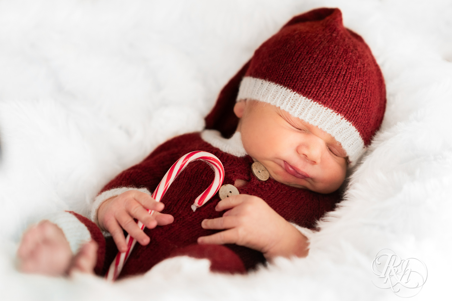 Biracial baby dressed in Santa outfit holds candy cane during family photography in Burnsville, Minnesota.