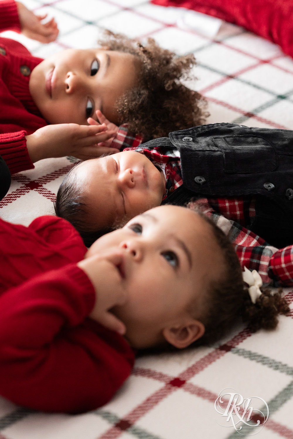 Little boy and girl in red sweaters smile at camera with their newborn brother during photography in Burnsville, Minnesota.