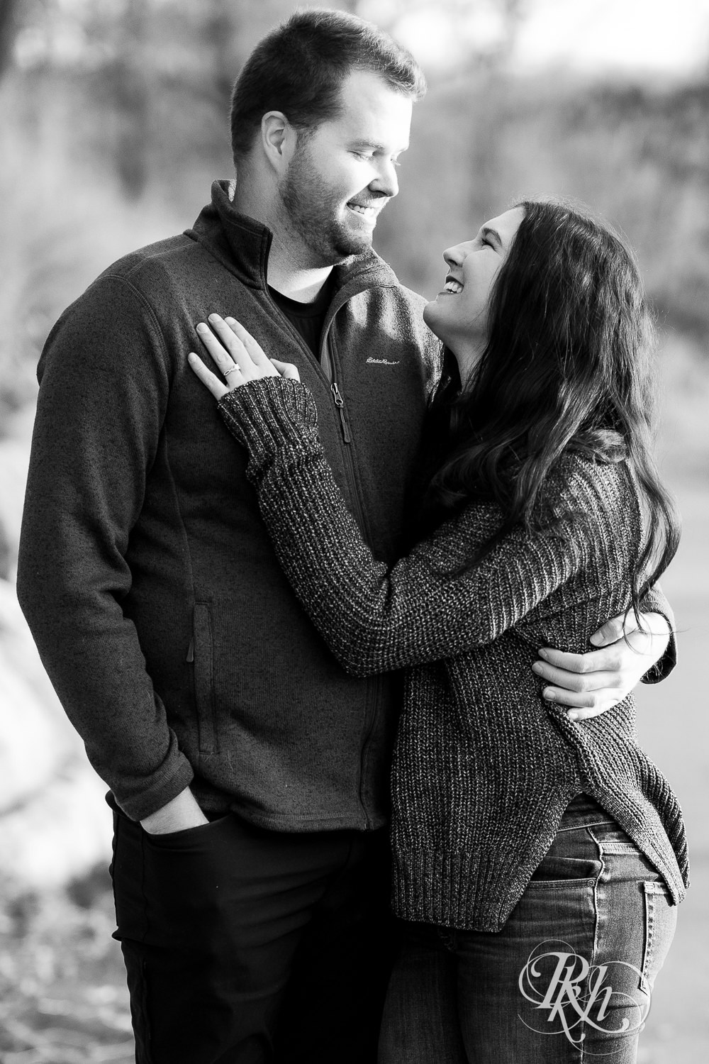 Man and woman smile and snuggle during winter engagement photography at Lebanon Hills in Eagan, Minnesota.