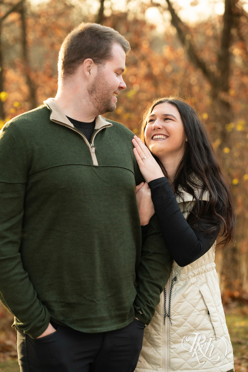Man and woman smile at each other during chilly November engagement photography at Lebanon Hills in Eagan, Minnesota.