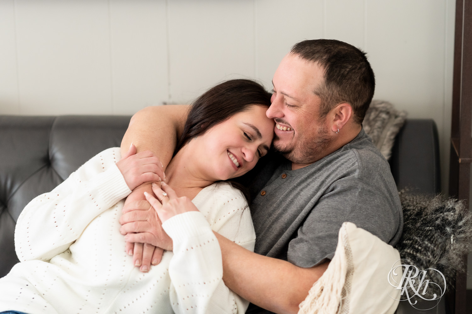 Man and woman in jeans and sweaters snuggle on a couch during cabin engagement photos in Pine City, Minnesota.
