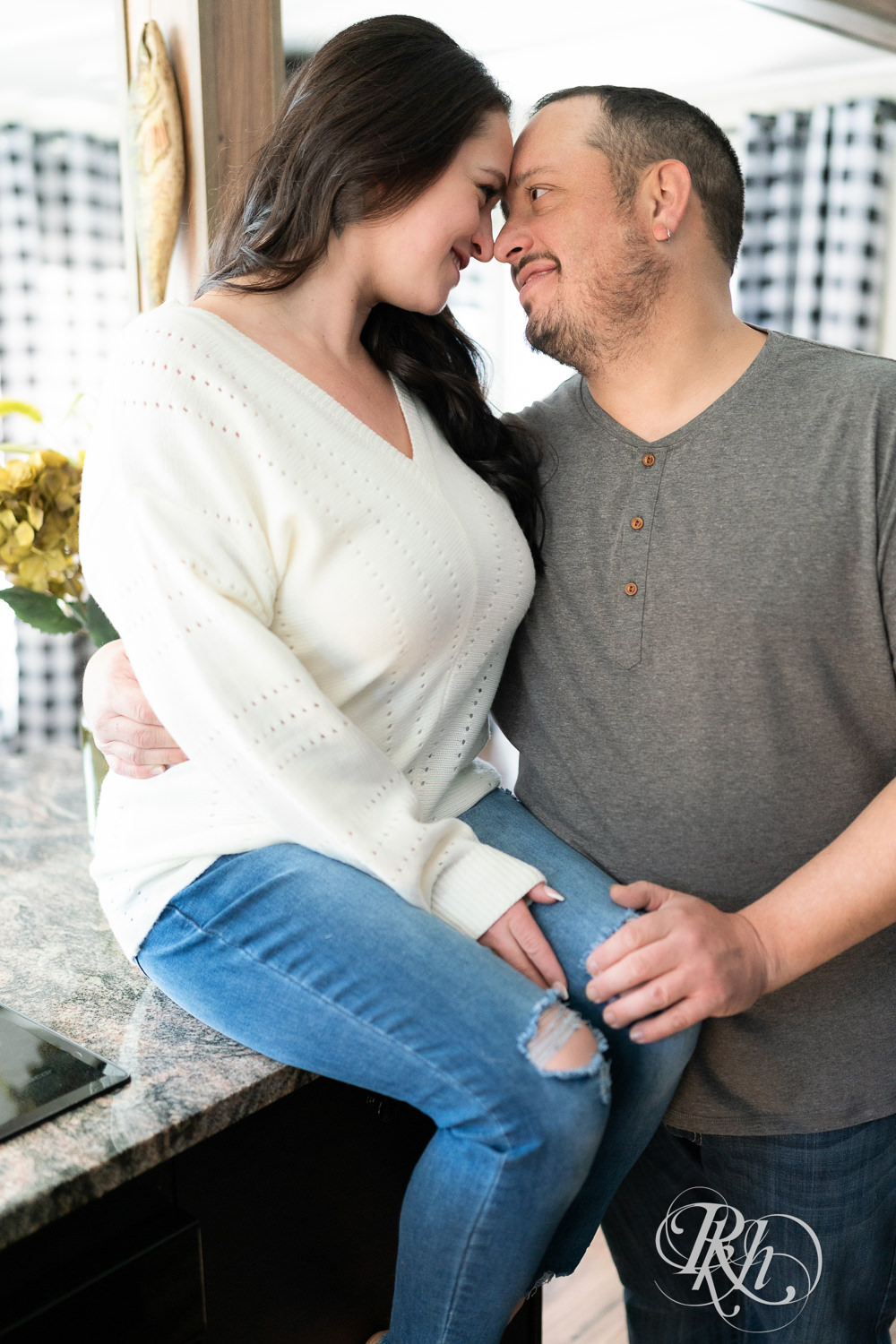 Man and woman in jeans and sweaters smile in a cabin in Pine City, Minnesota during engagement photography.