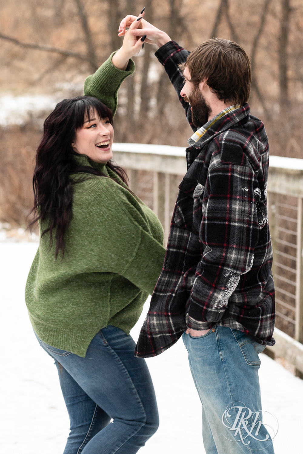 Man in flannel and woman in green sweater and jeans dance snowy bridge at Lebanon Hills in Eagan, Minnesota.