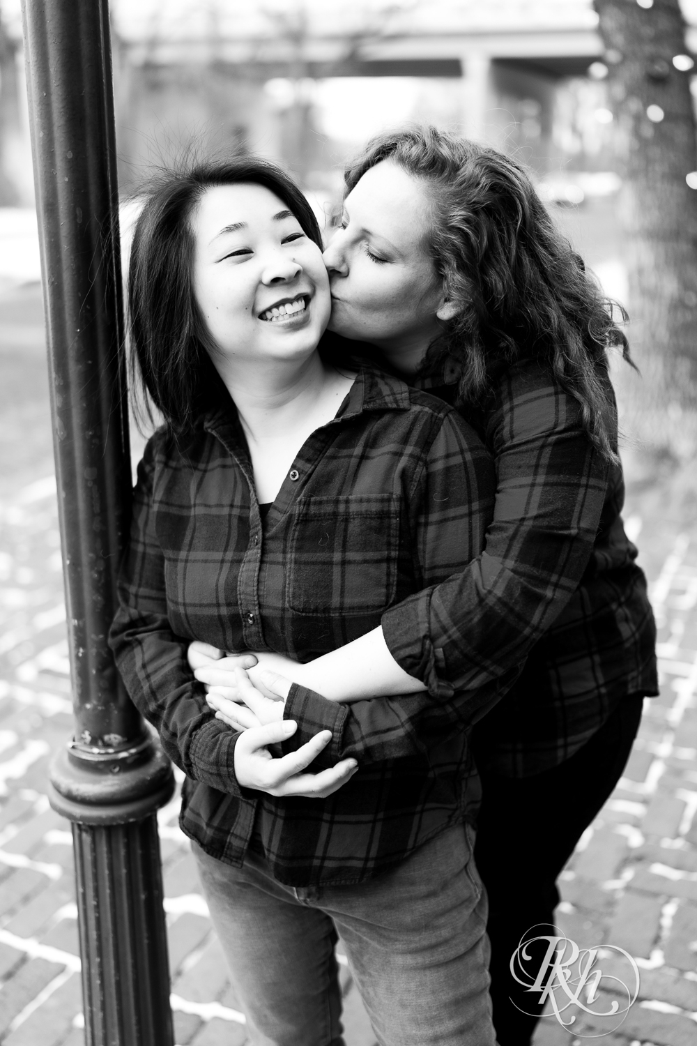 Red headed woman and Asian woman in red flannels kiss during winter engagement photography in Minneapolis, Minnesota.
