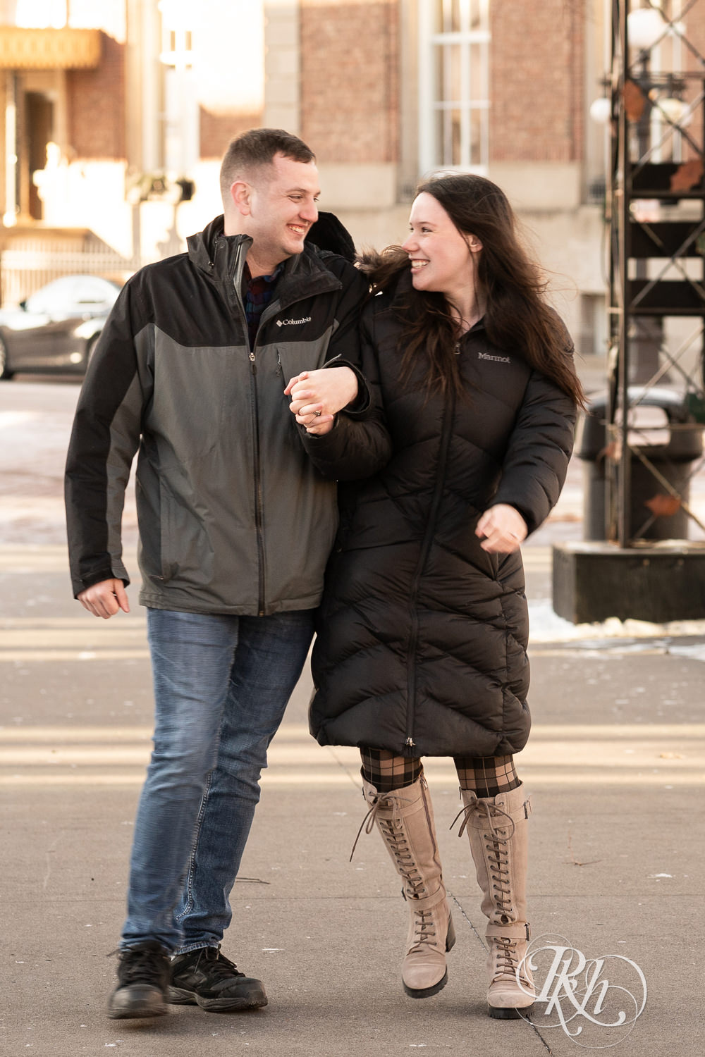 Man and woman in jackets walk and laugh in Saint Paul, Minnesota during winter engagement session.