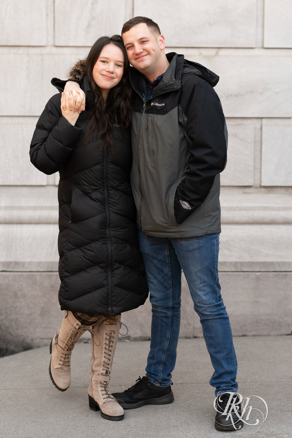 Man and woman in jackets smile in front of the Saint Paul Library in Saint Paul, Minnesota during winter engagement session.
