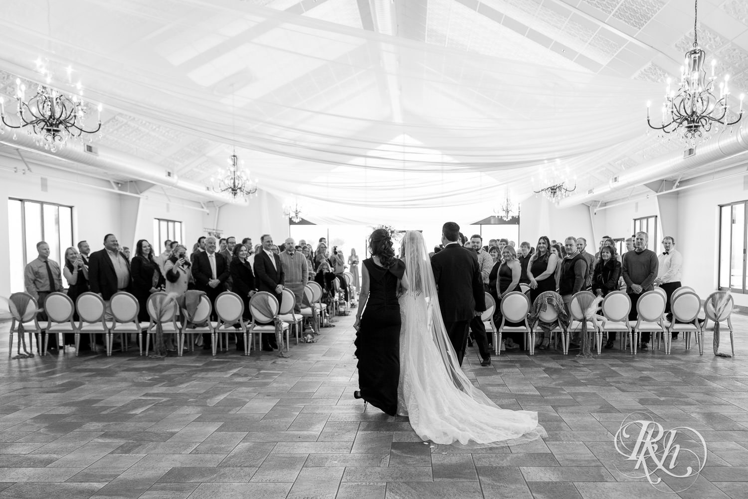 Bride walks down the aisle with parents during wedding ceremony at Bavaria Downs in Chaska, Minnesota.