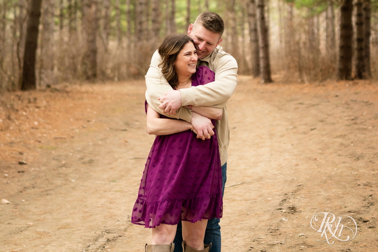 Man in jeans and woman in magenta dress laugh and hug in the woods in Lebanon Hills in Eagan, Minnesota.