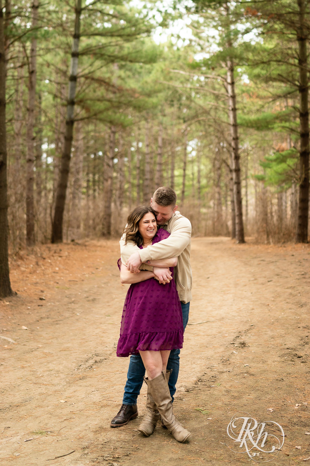 Man in jeans and woman in magenta dress laugh and hug in the woods in Lebanon Hills in Eagan, Minnesota.