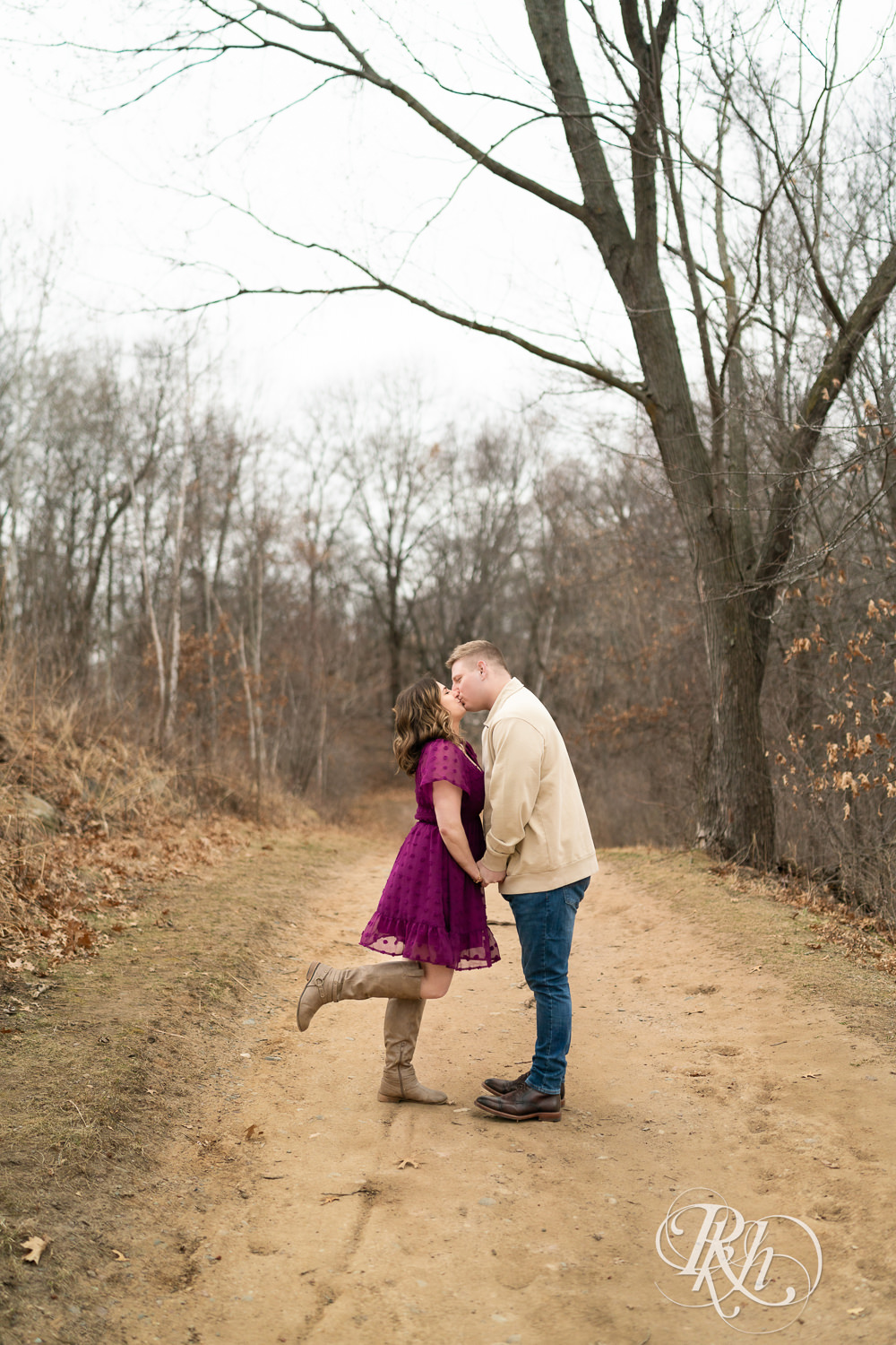 Man in jeans and woman in magenta dress kiss on a trail during March engagement photography in Eagan, Minnesota.