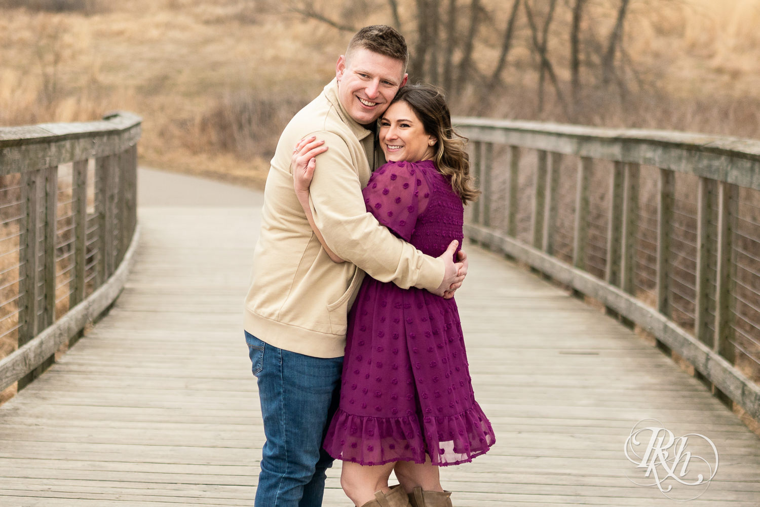 Man in jeans and woman in magenta dress smile on a bridge during March engagement photography in Eagan, Minnesota.