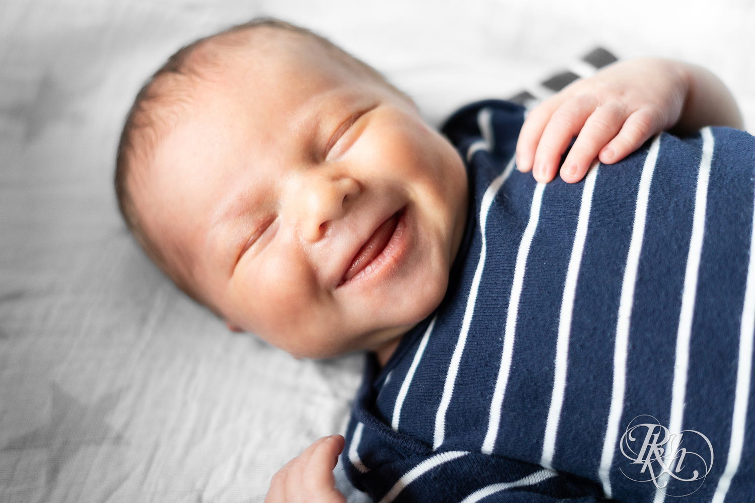 Baby dressed in stripped shirt smiles during newborn photography session in Ham Lake, Minnesota.