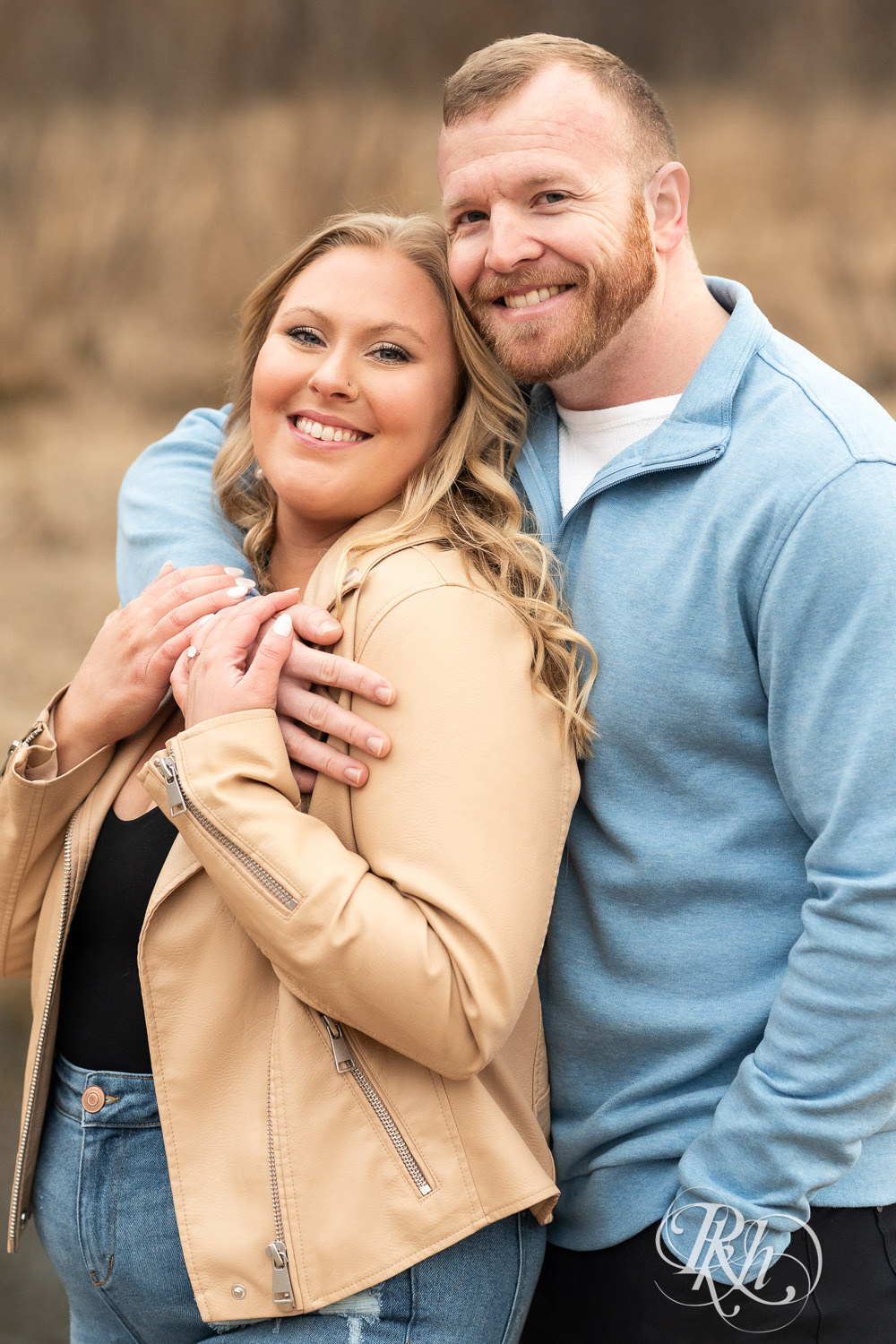 Man in blue shirt and woman in jeans smile during engagement photography at Rice Creek Regional Trail in Shoreview, Minnesota.