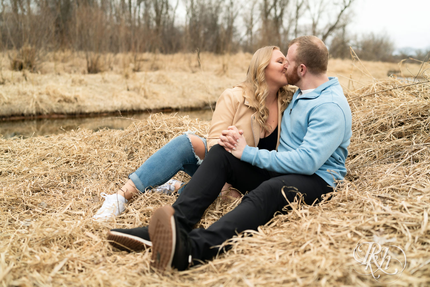 Man in blue shirt and woman in jeans kiss during engagement photography at Rice Creek Regional Trail in Shoreview, Minnesota.