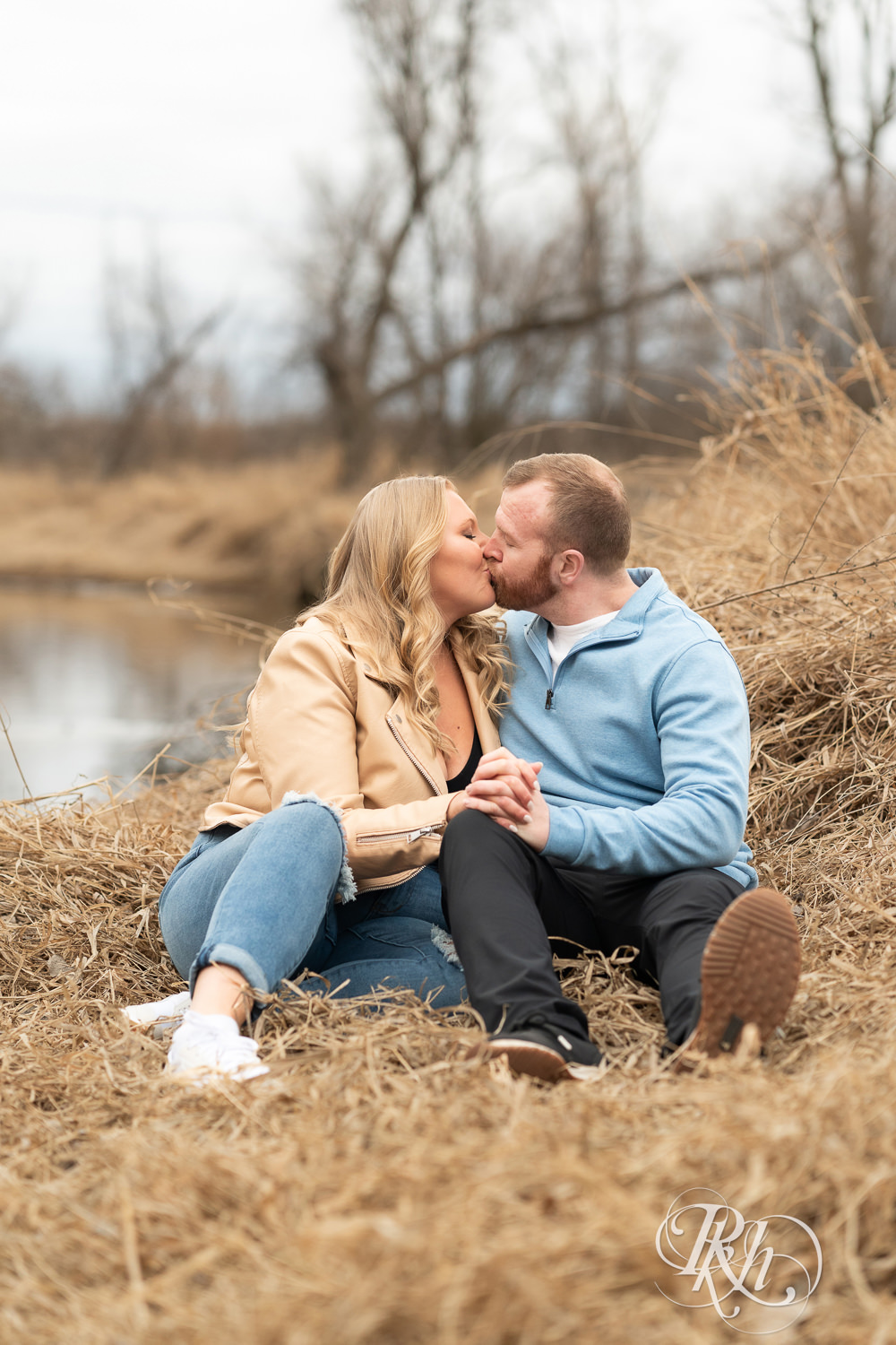 Man in blue shirt and woman in jeans kiss during engagement photography at Rice Creek Regional Trail in Shoreview, Minnesota.