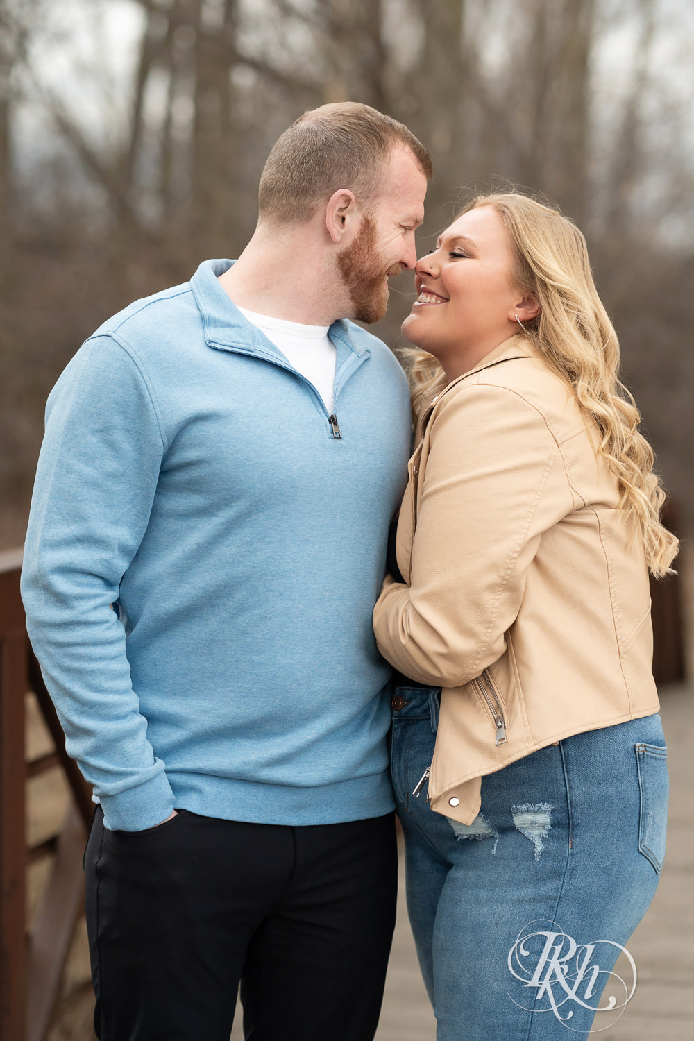 Man in blue shirt and woman in jeans smile during engagement photography at Rice Creek North Regional Trail in Shoreview, Minnesota.