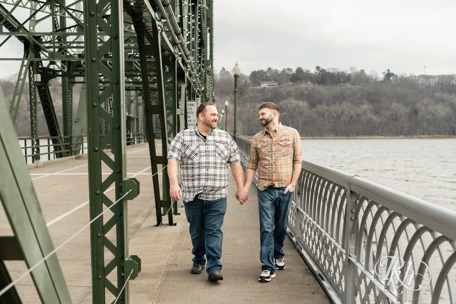 Two men in flannels and jeans walk in on the bridge during engagement photography in Stillwater, Minnesota.