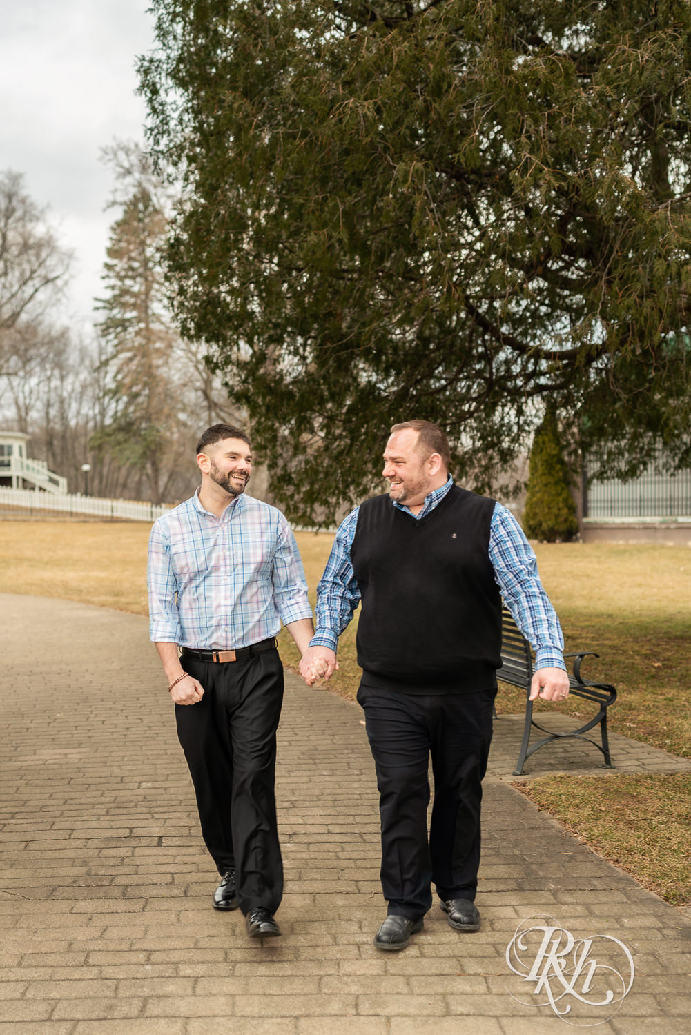 Two men in plaid shirts laugh while walking during engagement photography at Pioneer Park in Stillwater, Minnesota.