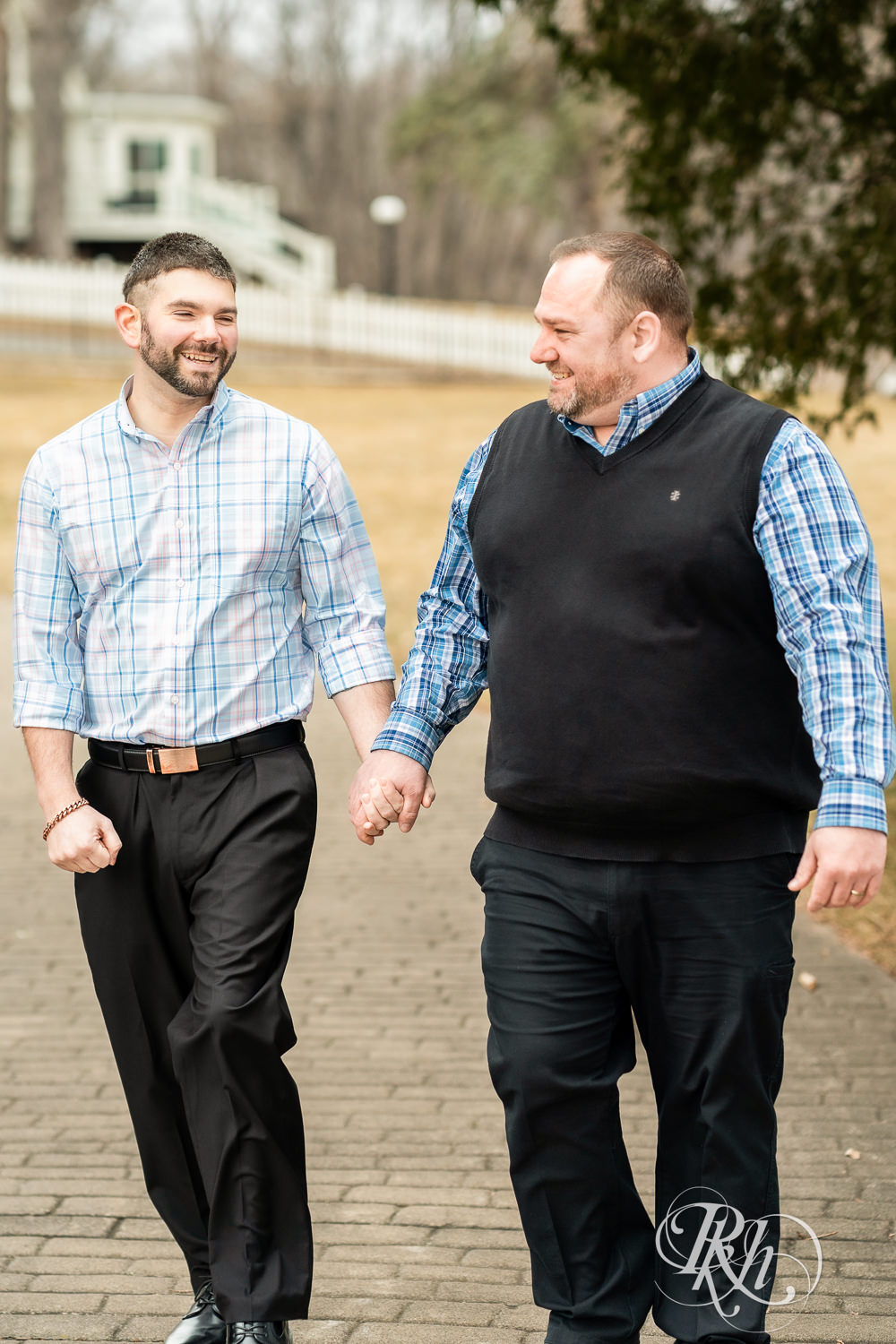 Two men in plaid shirts laugh while walking during engagement photography at Pioneer Park in Stillwater, Minnesota.