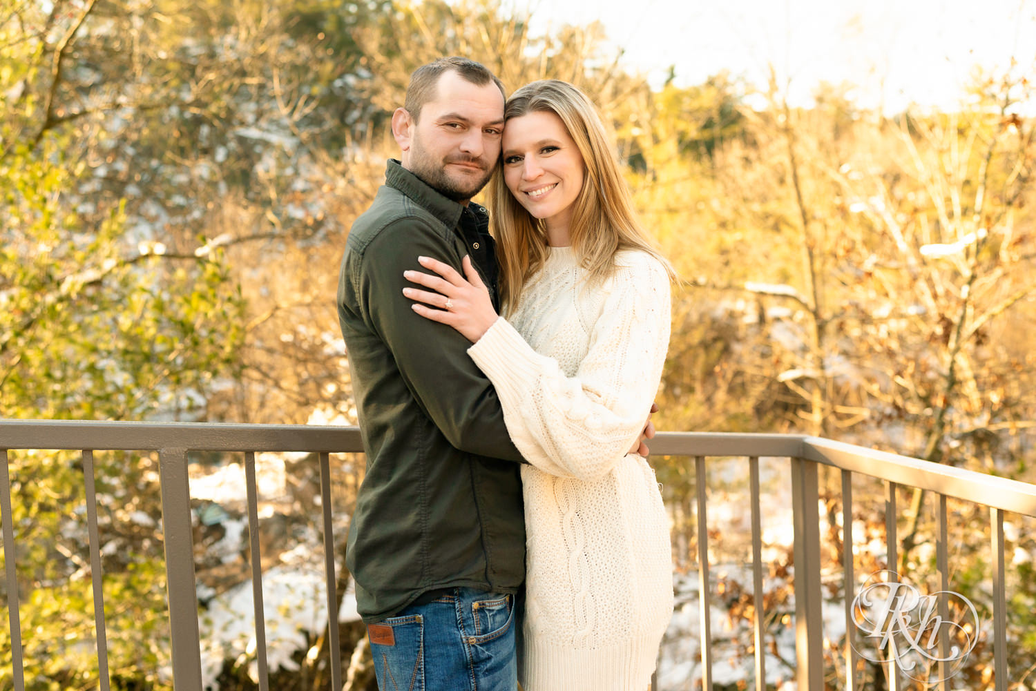 Man in jeans and green shirt and woman in a white sweater smile in the snow at sunrise during Taylor's Falls engagement photography session.