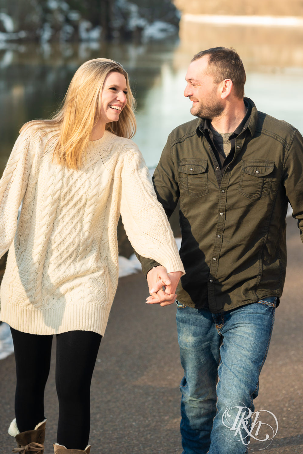 Man in jeans and green shirt and woman in a white sweater smile while walking during Taylor's Falls engagement photography session.