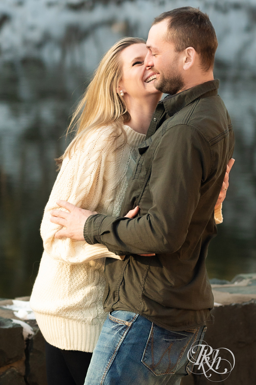 Man in jeans and green shirt and woman in a white sweater laugh during Taylor's Falls engagement photography session.