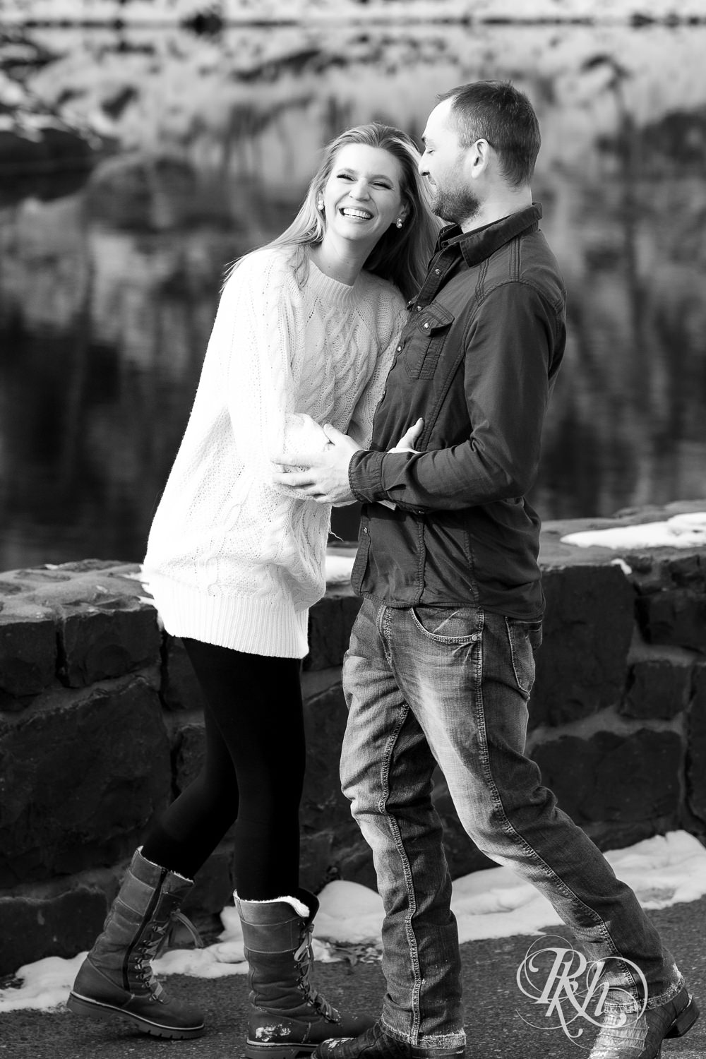 Man in jeans and green shirt and woman in a white sweater laugh during Taylor's Falls engagement photography session.