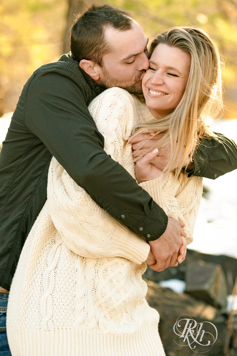Man in jeans and green shirt and woman in a white sweater smile laugh at winter engagement photography session in Taylors Falls, Minnesota.