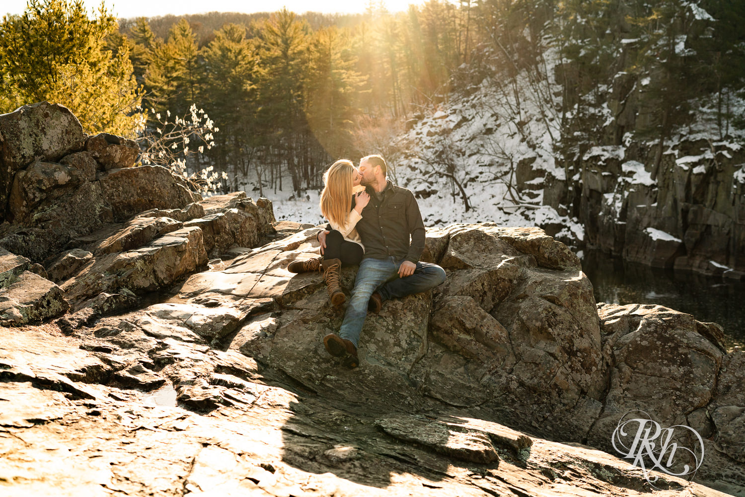 Man in jeans and green shirt and woman in a white sweater kiss during sunrise engagement photography session in Taylors Falls, Minnesota.