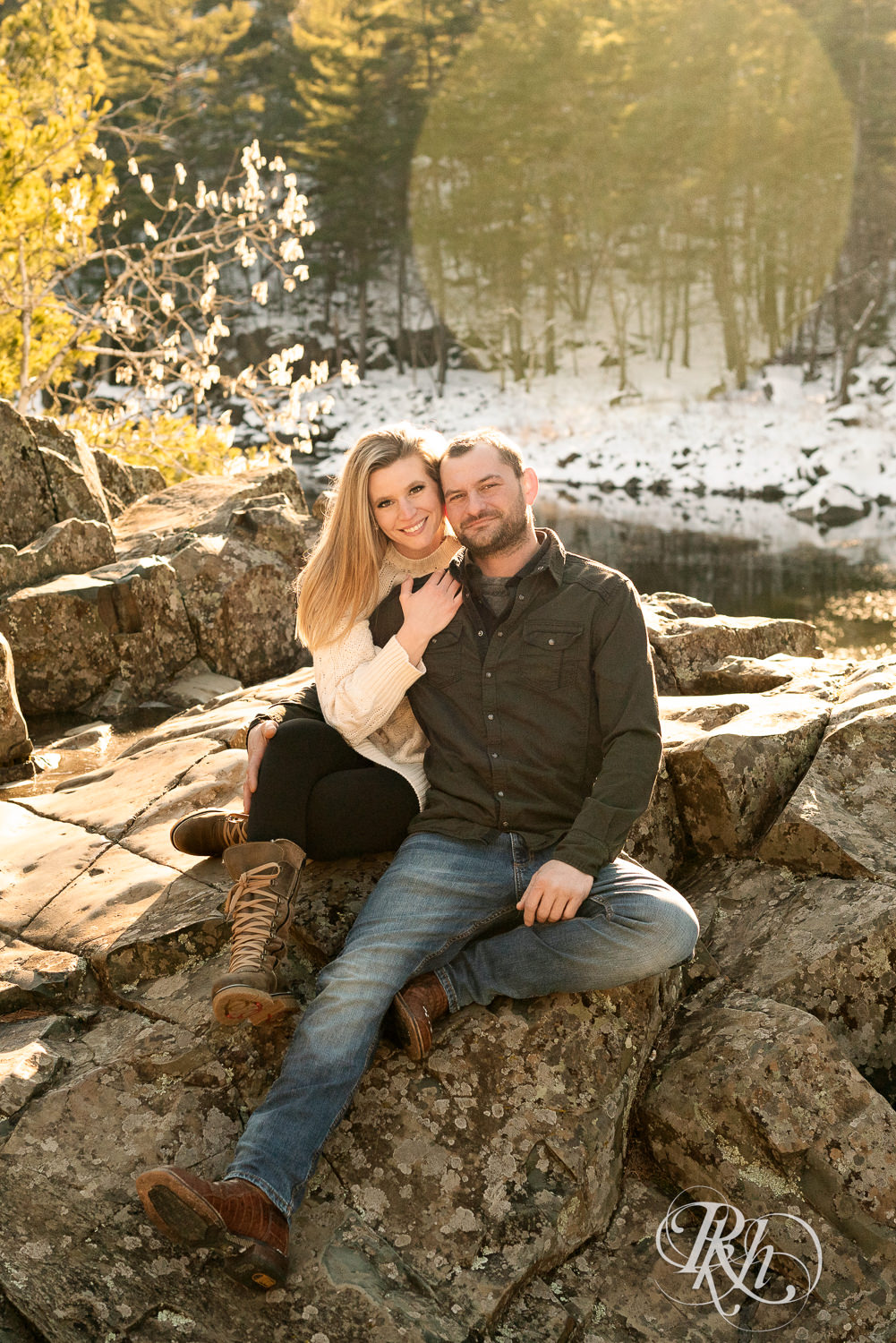 Man in jeans and green shirt and woman in a white sweater smile during sunrise engagement photography session in Taylors Falls, Minnesota.