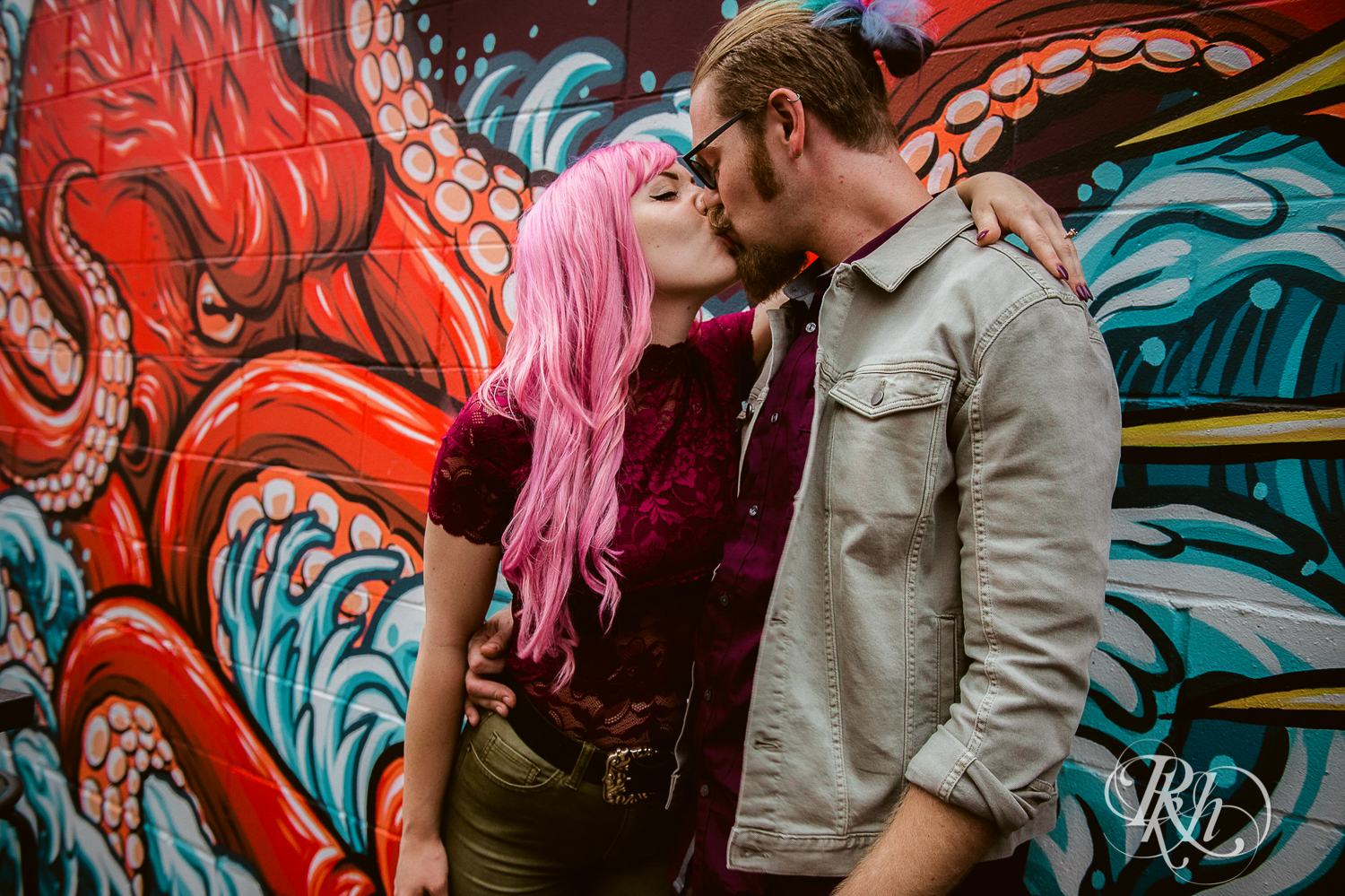 Girl with pink hair kissing man in alley.
